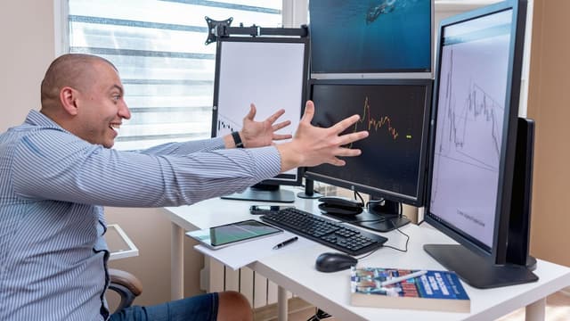 Trader comemorando diante de quatro monitores com gráficos