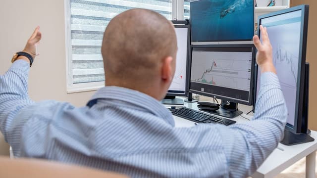 Trader operando em setup com quatro telas de gráficos