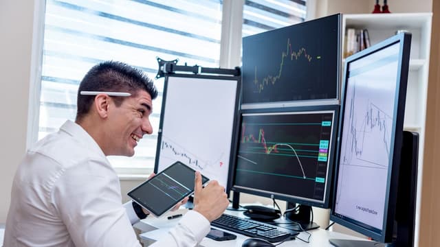 Trader analisando o mercado com tablet e múltiplas telas
