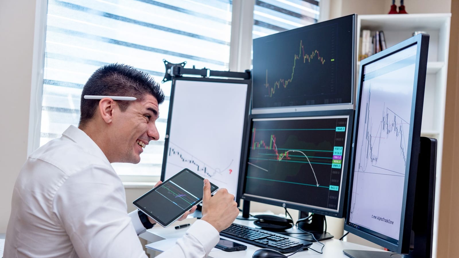Trader analisando o mercado com tablet e múltiplas telas