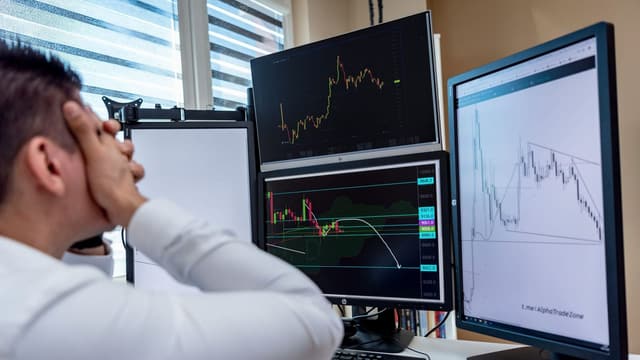 Trader concentrado observando três telas de gráficos